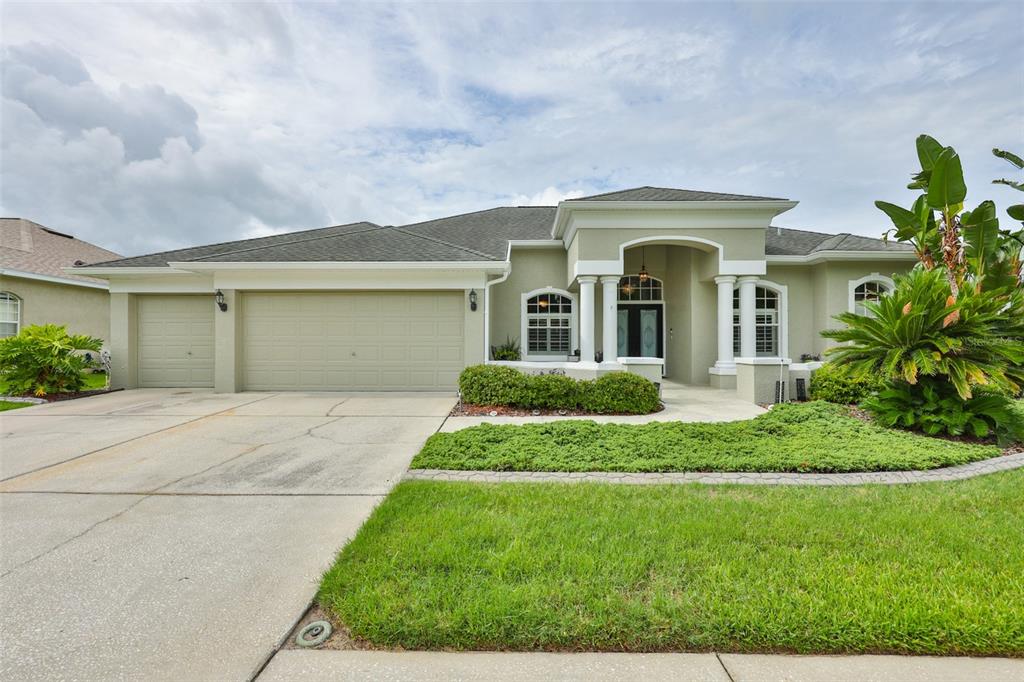A single-story house with a light green exterior, a three-car garage, and a columned entryway — 7521 MELOGOLD CIRCLE, LAND O LAKES, FL