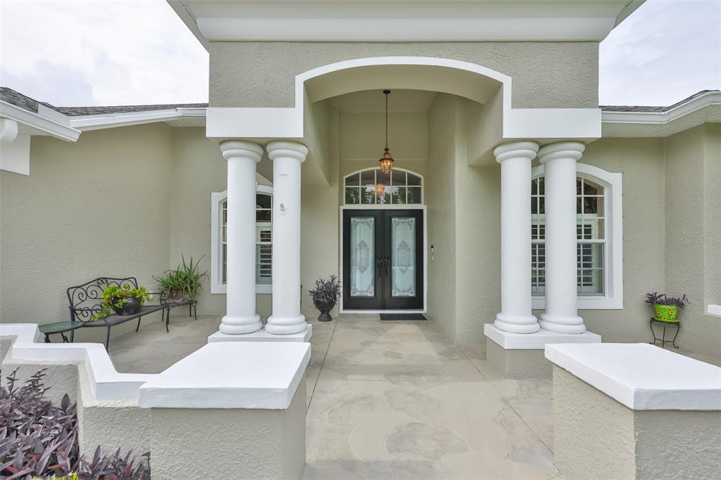 The front entrance features a covered porch with four white columns and double glass doors — 7521 MELOGOLD CIRCLE, LAND O LAKES, FL