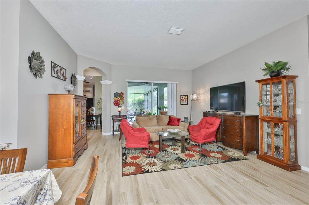 A living room features light wood-look tile flooring, red armchairs, and a beige sofa — 7521 MELOGOLD CIRCLE, LAND O LAKES, FL