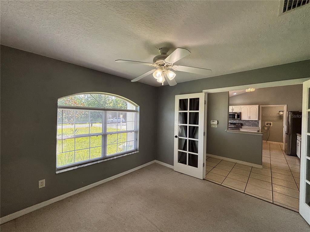 A carpeted room with a ceiling fan, arched window, and French doors opening to a kitchen — 37 WHIPPOORWILL DRIVE, PALM COAST, FL