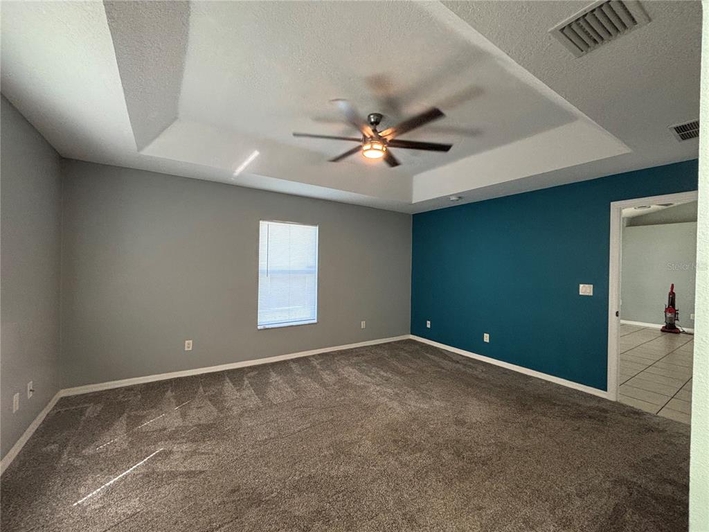 A bedroom features gray walls, a teal accent wall, carpeted flooring, and a tray ceiling — 37 WHIPPOORWILL DRIVE, PALM COAST, FL