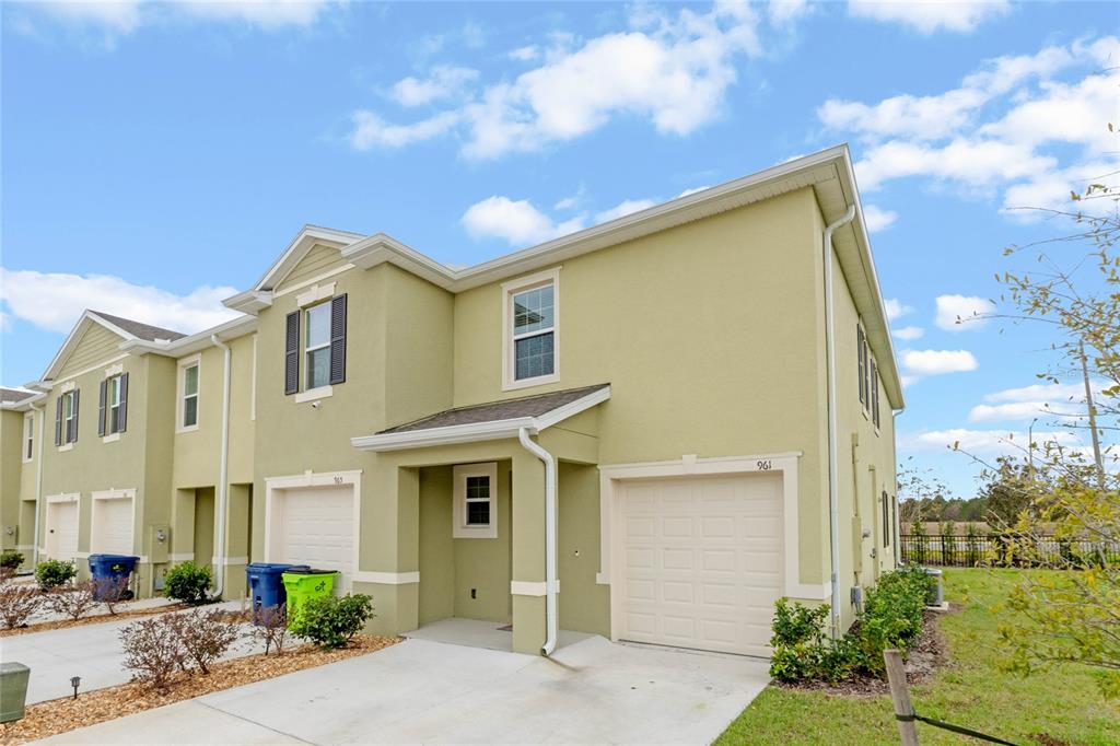 A two-story townhouse with light green stucco siding, a single-car garage, and a concrete driveway — 961 LIDO DRIVE, HOWEY IN THE HILLS, FL