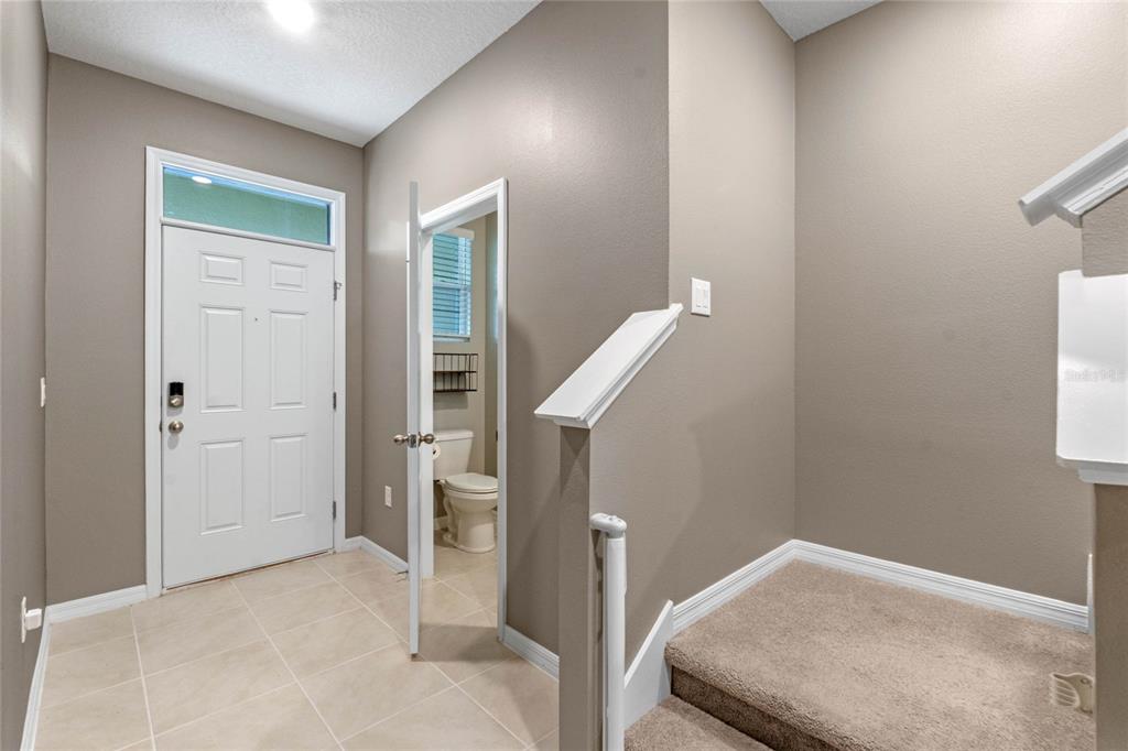An entryway features tile flooring, a white front door, a half bathroom, and carpeted stairs — 961 LIDO DRIVE, HOWEY IN THE HILLS, FL