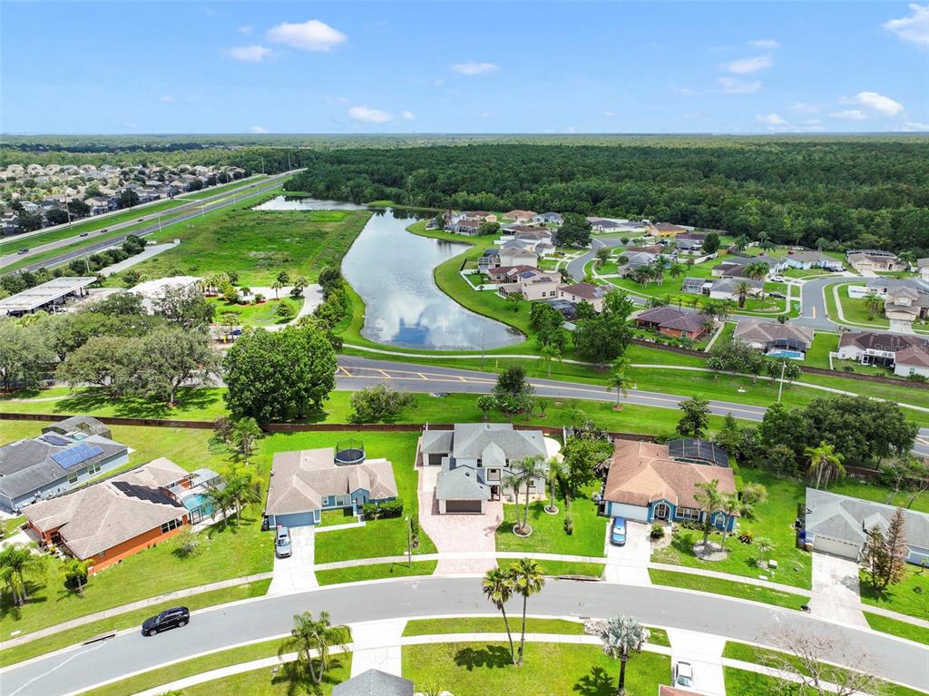 An aerial view shows a suburban neighborhood with houses, a central pond, and a highway — 2574 SAGE DRIVE, KISSIMMEE, FL