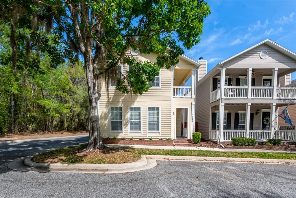 A two-story yellow house with a front porch and a large tree in the yard — 11688 NW 17TH PLACE, GAINESVILLE, FL