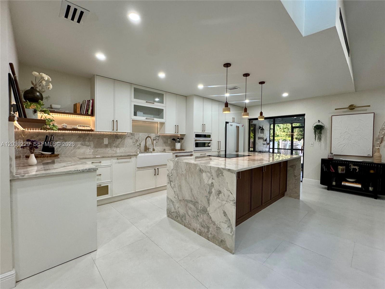 A modern kitchen features white cabinetry, a marble-topped island, and dark wood accents — 172 Wild Pine Rd, Wellington FL 33414, WELLINGTON, FL