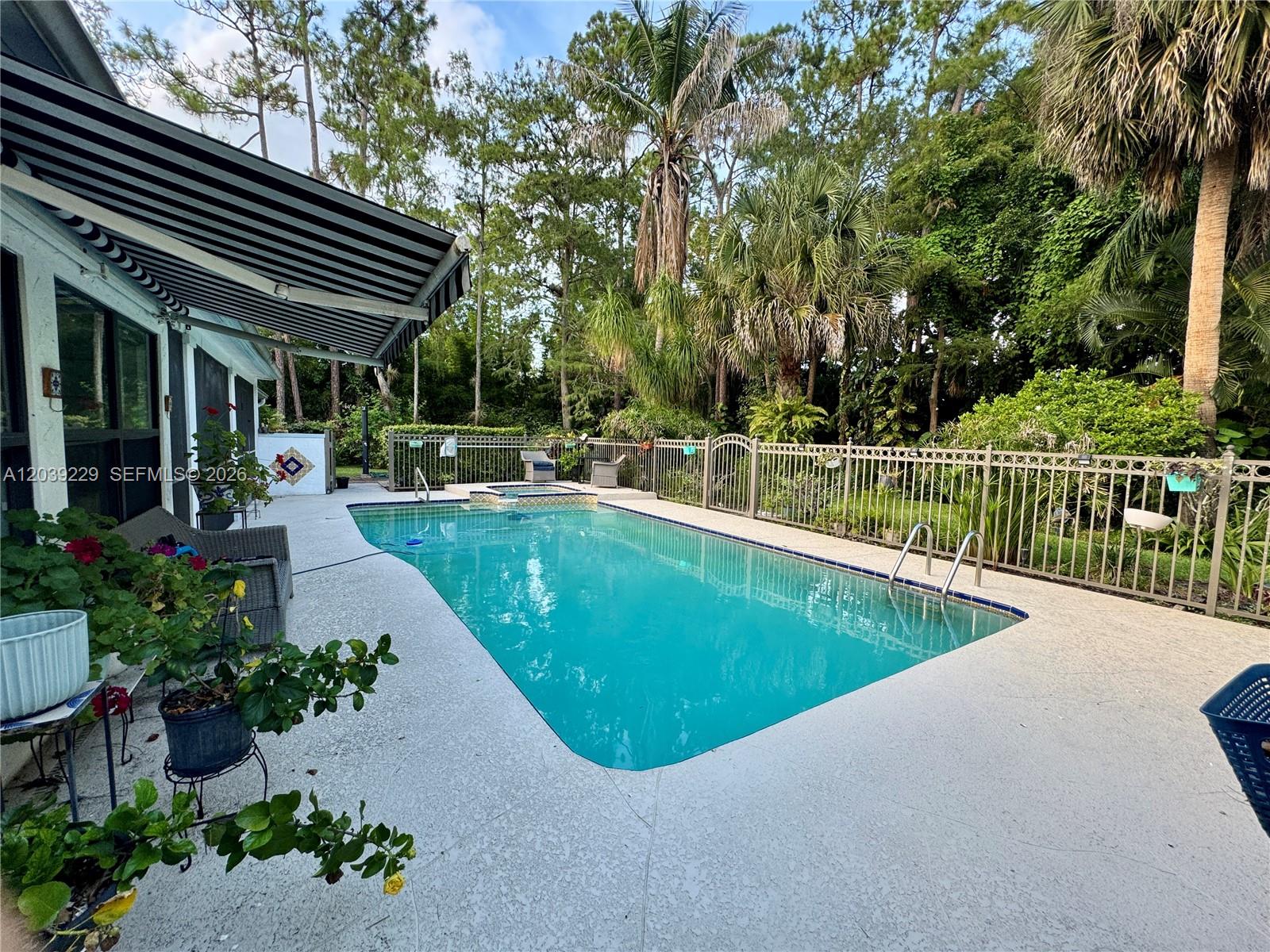 A rectangular swimming pool sits on a patio next to a house with an awning — 172 Wild Pine Rd, Wellington FL 33414, WELLINGTON, FL