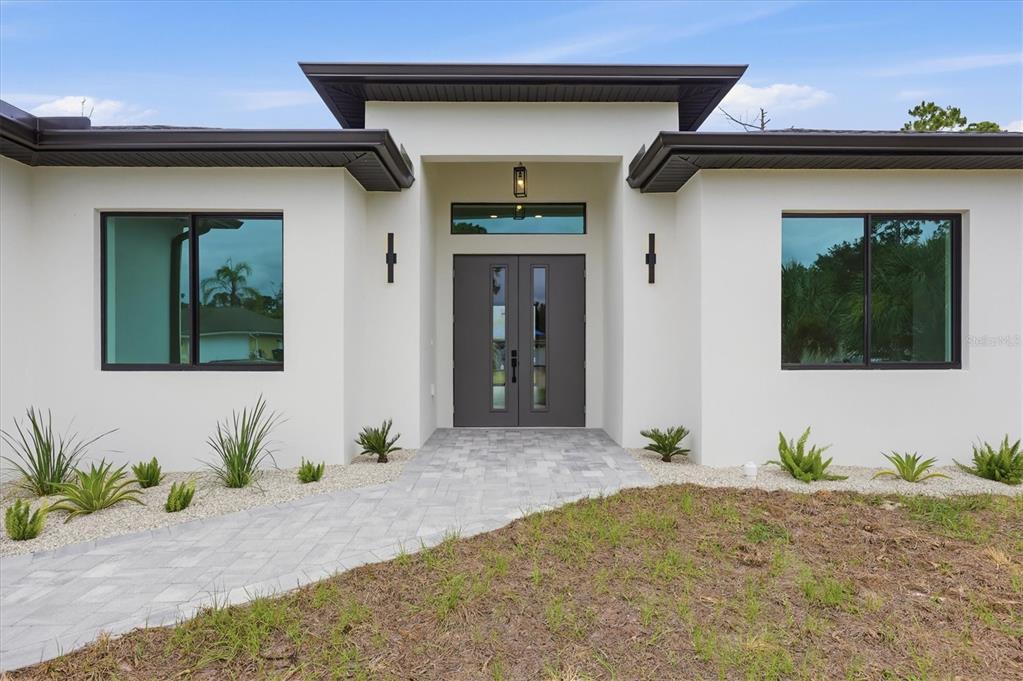 A modern white house exterior features a double front door, dark trim, and stone walkway — 3638 LUBEC AVENUE, NORTH PORT, FL
