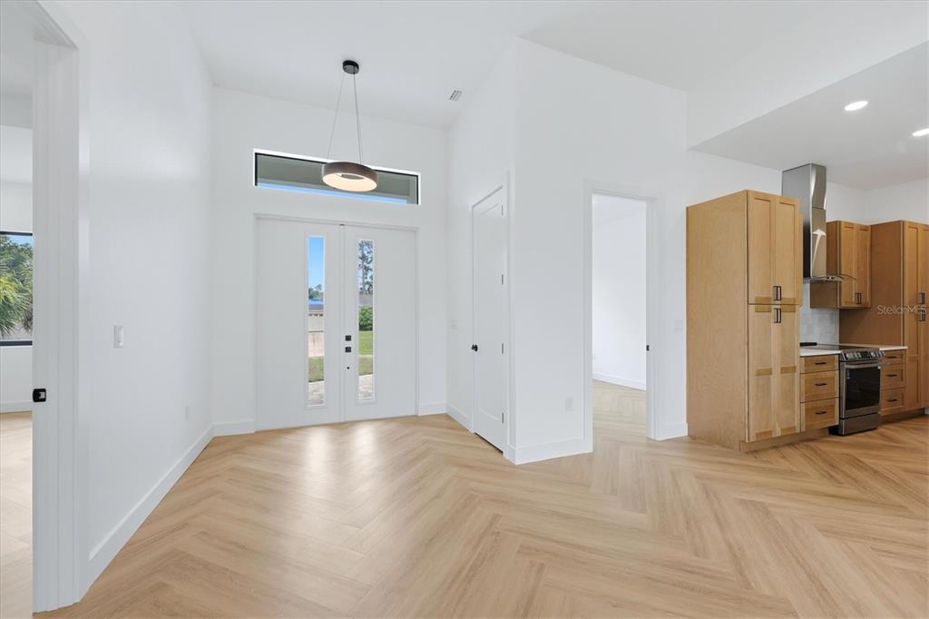 A bright entryway with herringbone wood floors leads to a kitchen with light wood cabinets — 3638 LUBEC AVENUE, NORTH PORT, FL