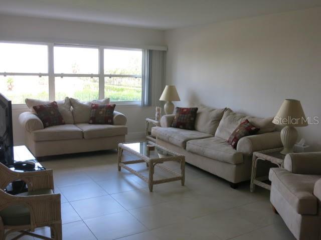 A living room features two beige sofas, a glass-topped coffee table, and large windows — 1230 GULF BOULEVARD UNIT 306, CLEARWATER BEACH, FL