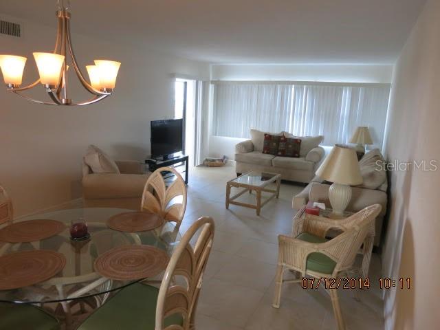 A dining area with a glass table and chandelier opens into a living room with seating — 1230 GULF BOULEVARD UNIT 306, CLEARWATER BEACH, FL