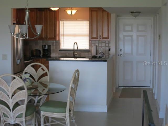 A dining area with a glass table and wicker chairs sits before a kitchen with cabinets — 1230 GULF BOULEVARD UNIT 306, CLEARWATER BEACH, FL
