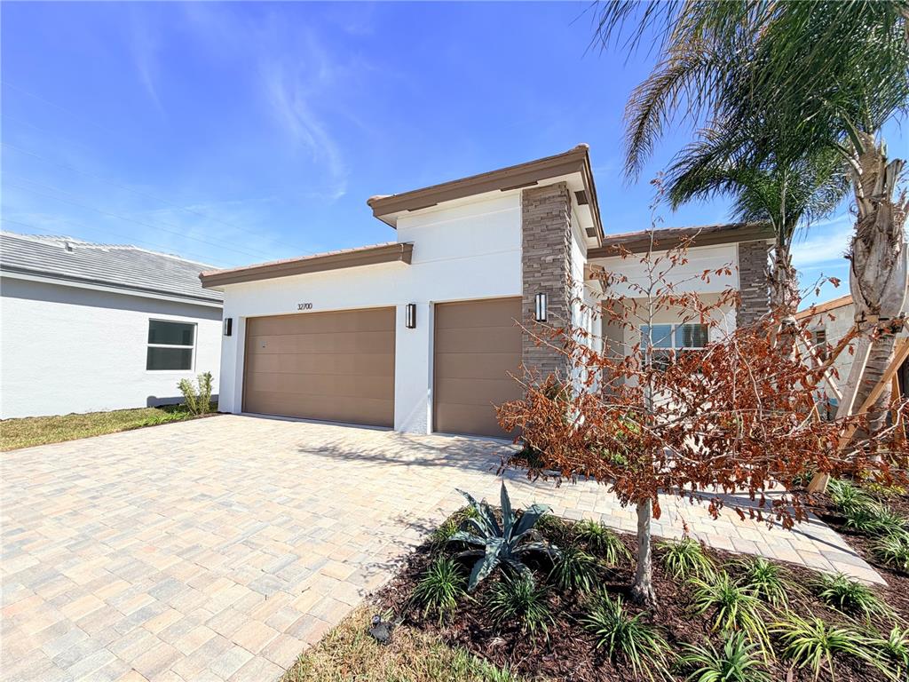 A modern single-story house features a two-car garage, stone accents, and a paved driveway — 32700 NEROLI STREET, WESLEY CHAPEL, FL