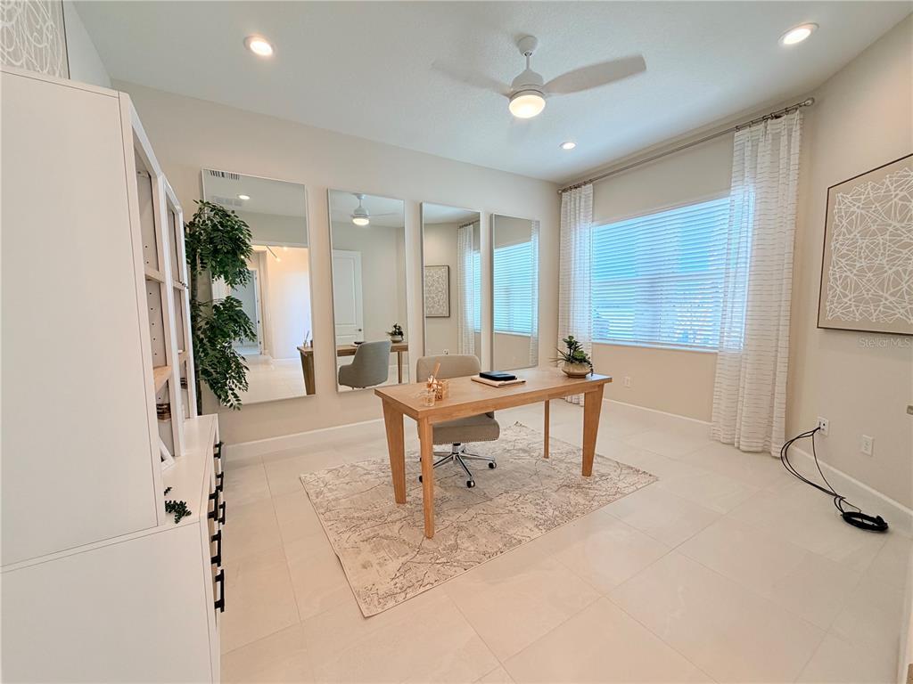 A home office features a wooden desk, a rug, three wall mirrors, and a ceiling fan — 32700 NEROLI STREET, WESLEY CHAPEL, FL
