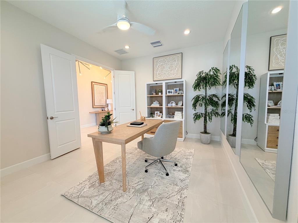 A home office features a wooden desk, a gray chair, shelving, and a mirrored wall — 32700 NEROLI STREET, WESLEY CHAPEL, FL