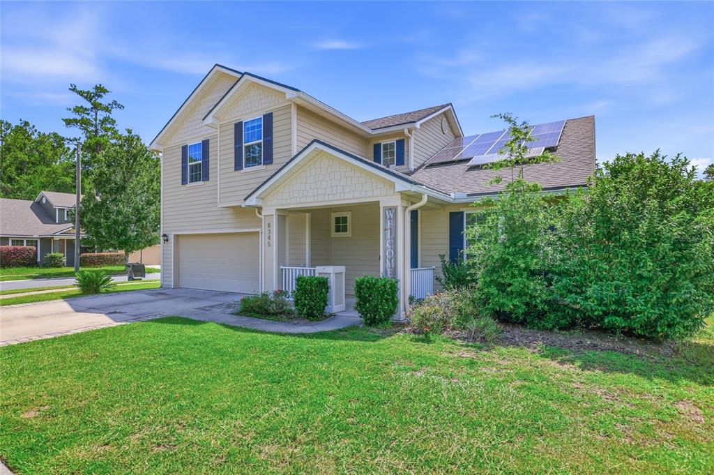 A two-story suburban house with beige siding, a two-car garage, and rooftop solar panels — 8345 NW 54TH TERRACE, GAINESVILLE, FL