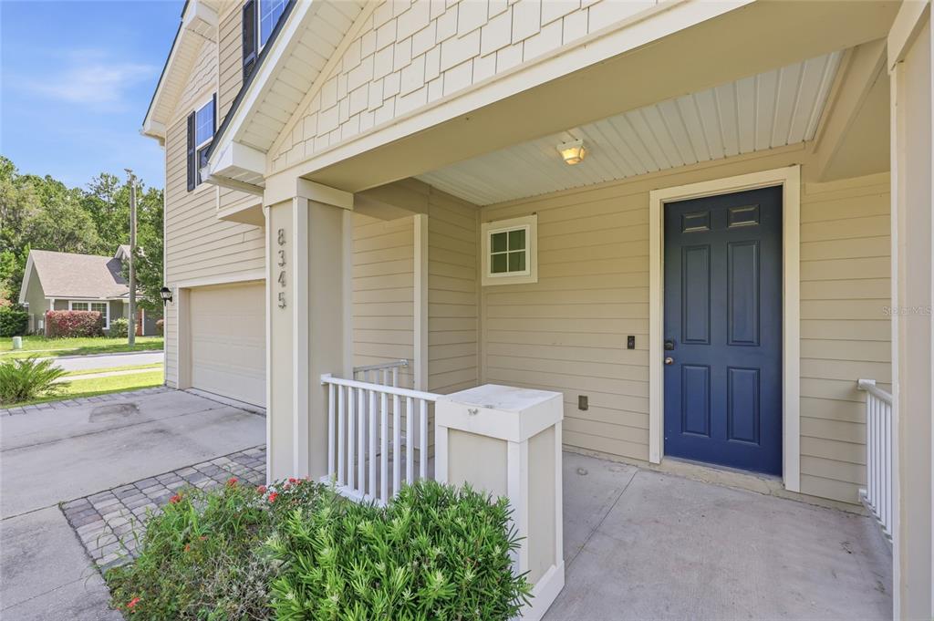 A tan house exterior features a covered porch, a blue front door, and a garage — 8345 NW 54TH TERRACE, GAINESVILLE, FL