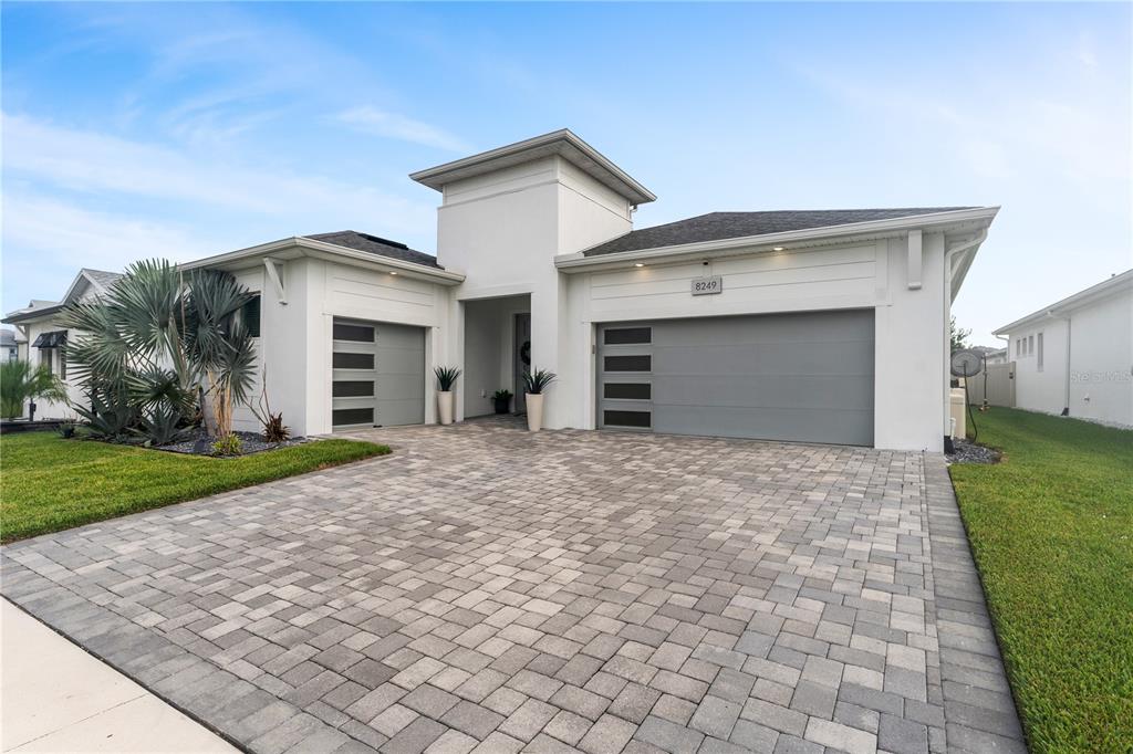 A modern single-story house features a paver driveway, two gray garage doors, and white siding — 8249 IVY STARK BOULEVARD, WESLEY CHAPEL, FL