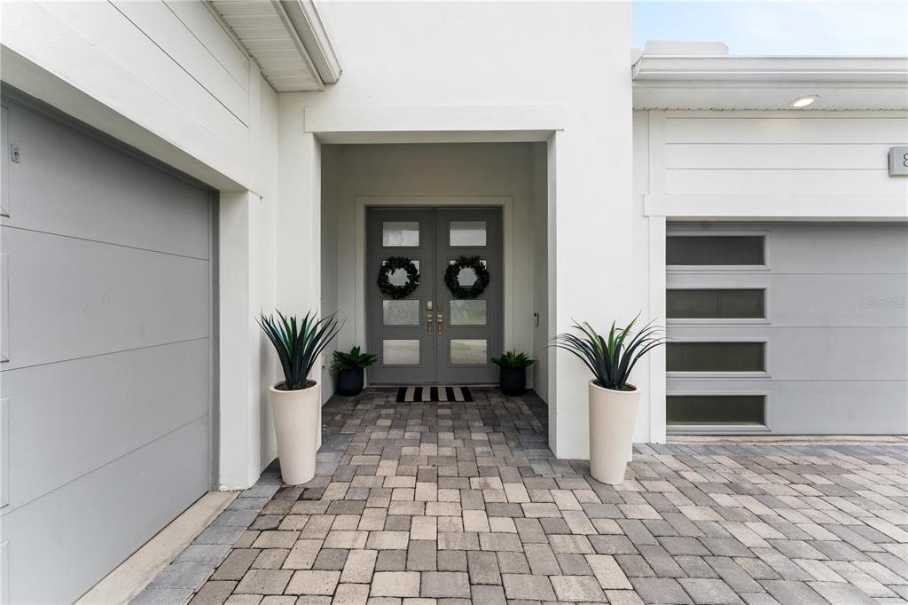 A modern home exterior features a gray double front door, paver driveway, and two garages — 8249 IVY STARK BOULEVARD, WESLEY CHAPEL, FL