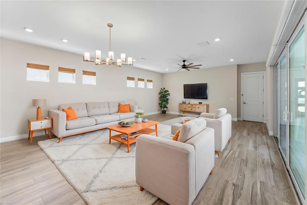 A living room features light-colored furniture, orange accents, a chandelier, and wood-look tile flooring — 8249 IVY STARK BOULEVARD, WESLEY CHAPEL, FL