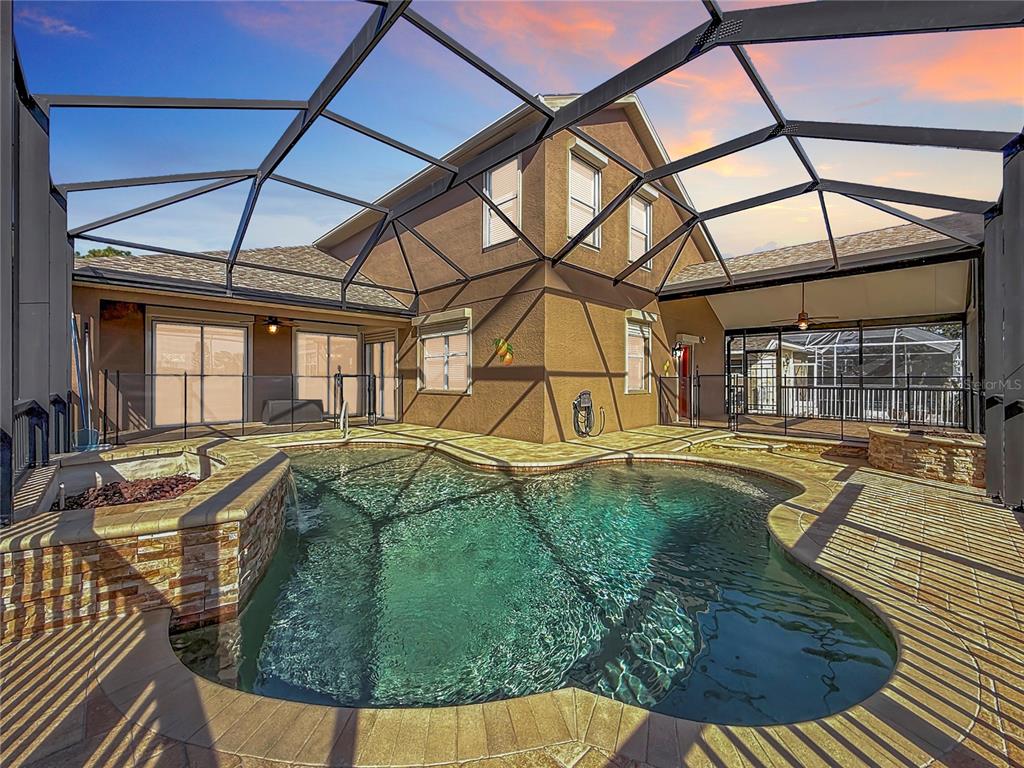 A swimming pool with a stone-accented spa sits inside a screened-in patio area — 4961 W BREEZE CIRCLE, PALM HARBOR, FL