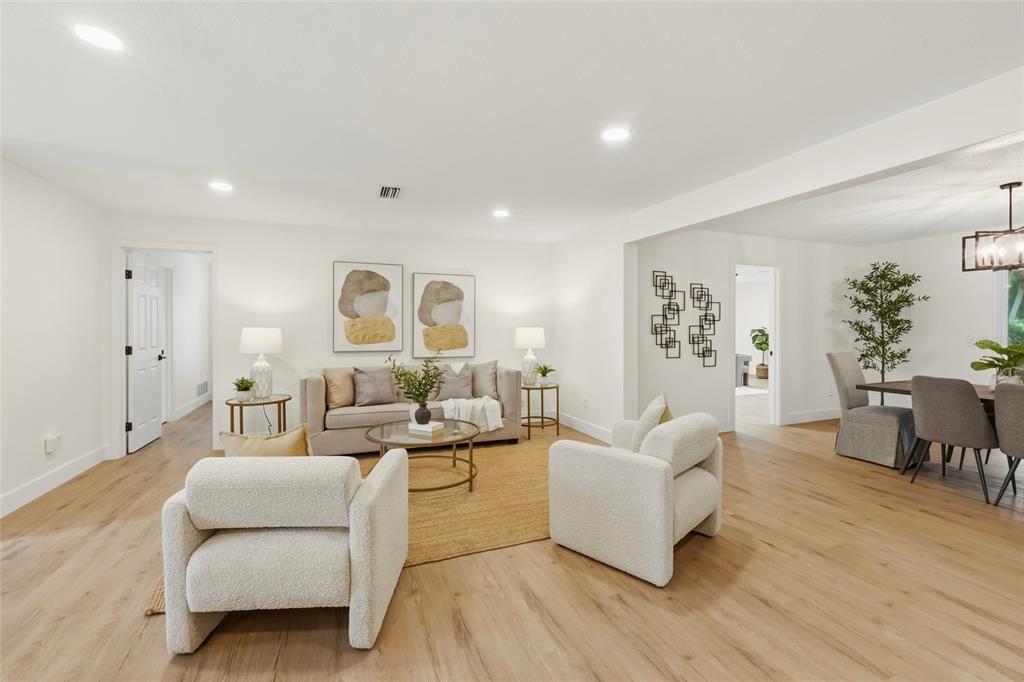 A bright living room features light wood floors, two white armchairs, and a neutral sofa — 435 MEHLENBACHER ROAD, LARGO, FL