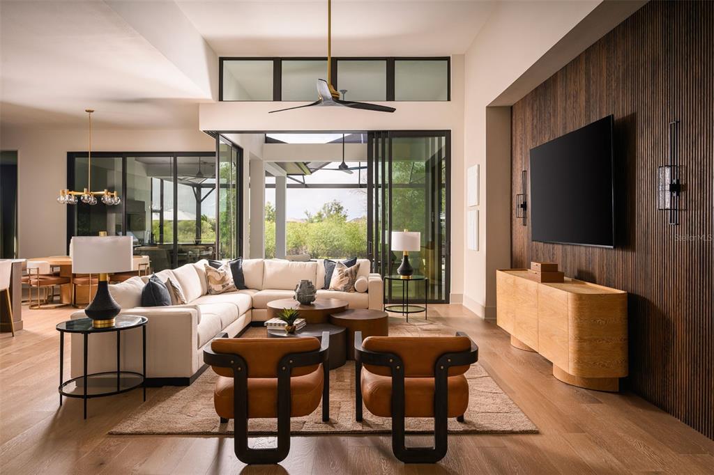 A modern living room features a sectional sofa, two leather chairs, and a wood-paneled wall — 8613 SANDPOINT STREET, SARASOTA, FL
