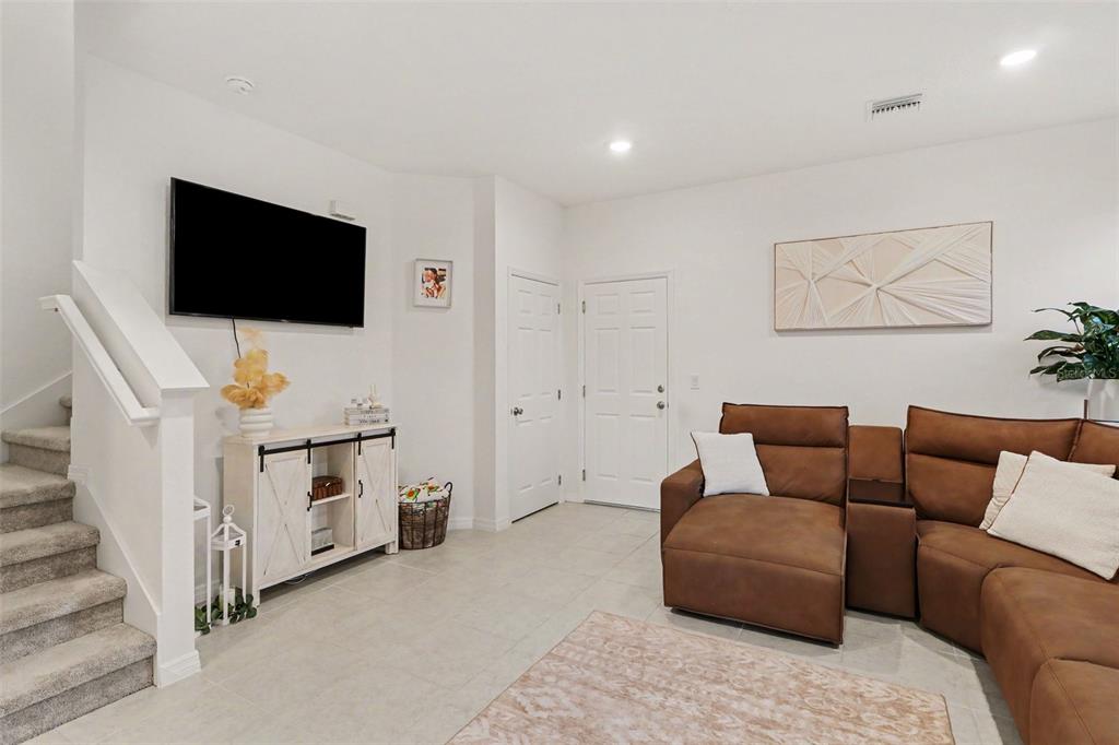 A living room features a large brown sectional sofa, a patterned rug, and white walls — 1180 WYCLIFFE WAY, ST CLOUD, FL