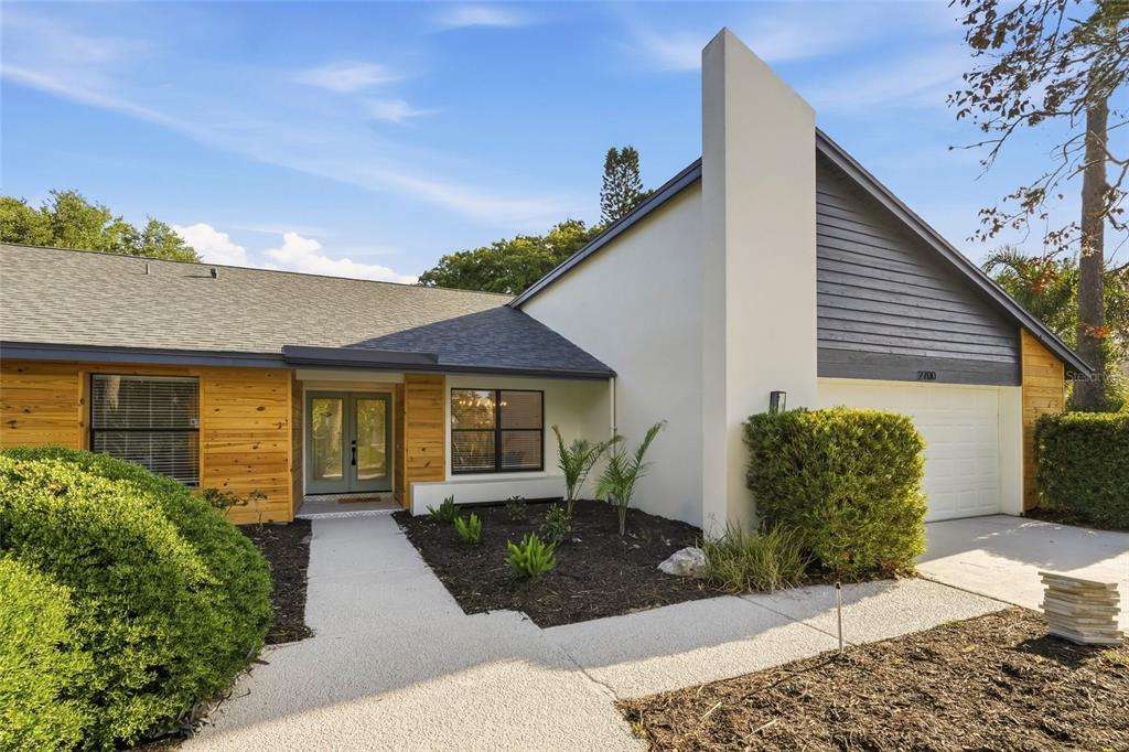 A single-story house with wood siding, a white stucco chimney, and a gray shingled roof — 2700 SEDGEFIELD COURT E, CLEARWATER, FL