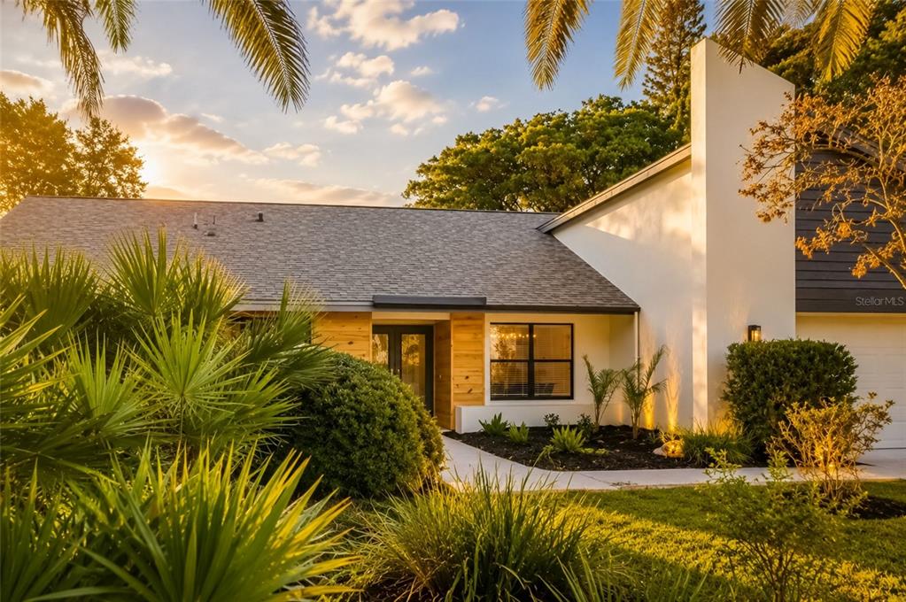 A single-story house with white walls, wood siding, a gray roof, and lush landscaping — 2700 SEDGEFIELD COURT E, CLEARWATER, FL