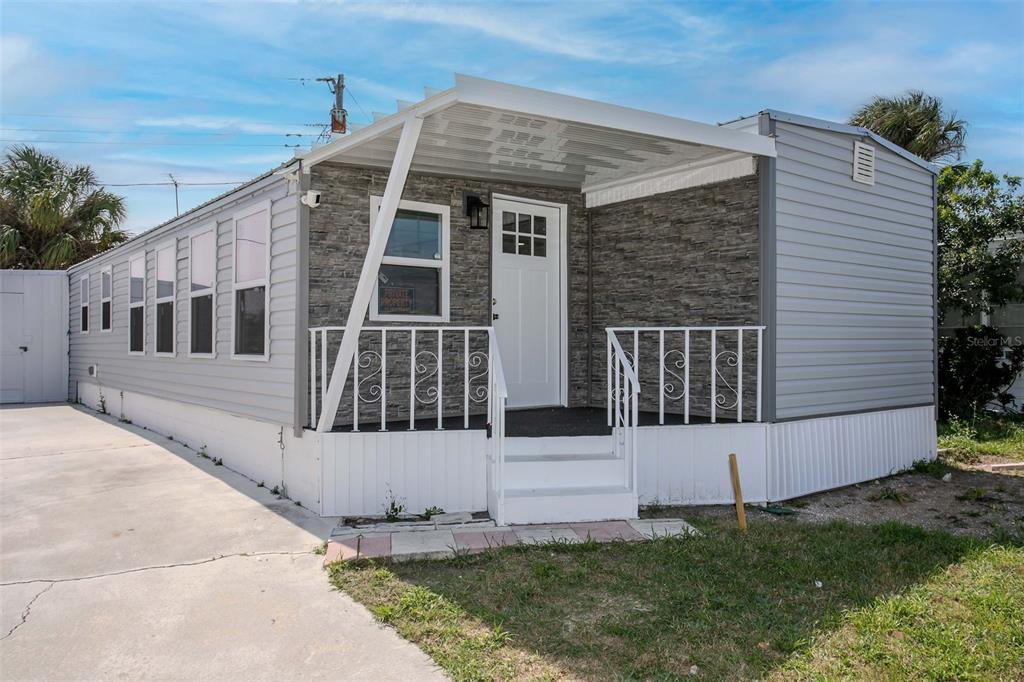 A single-story mobile home with gray siding, a stone-veneer facade, and a covered front porch — 410 W 51ST AVENUE DRIVE W, BRADENTON, FL