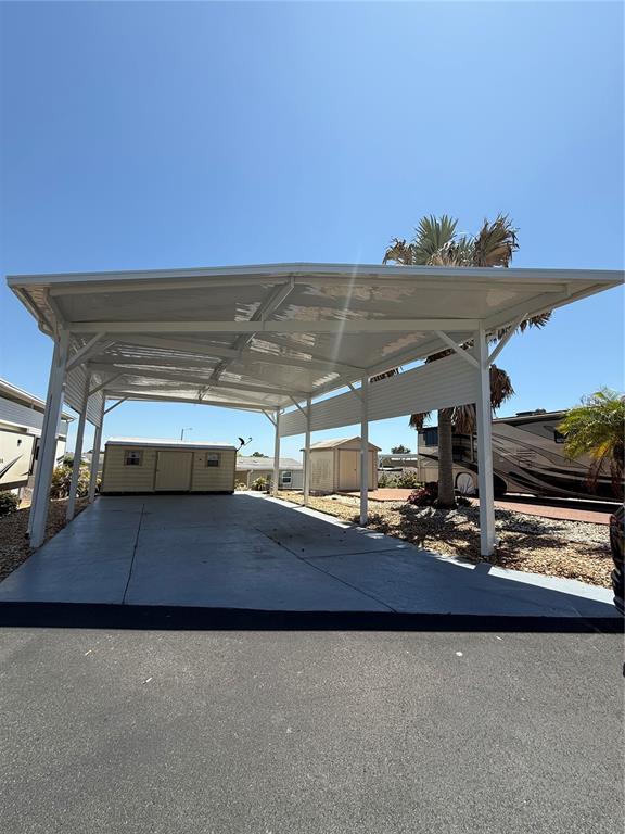 A large white metal carport covers a concrete driveway with two small storage sheds nearby — 319 BROKEN WOODS BOULEVARD, DAVENPORT, FL