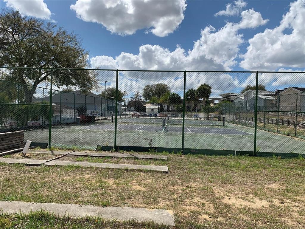 A fenced-in outdoor tennis court sits in a grassy area under a cloudy sky — 319 BROKEN WOODS BOULEVARD, DAVENPORT, FL