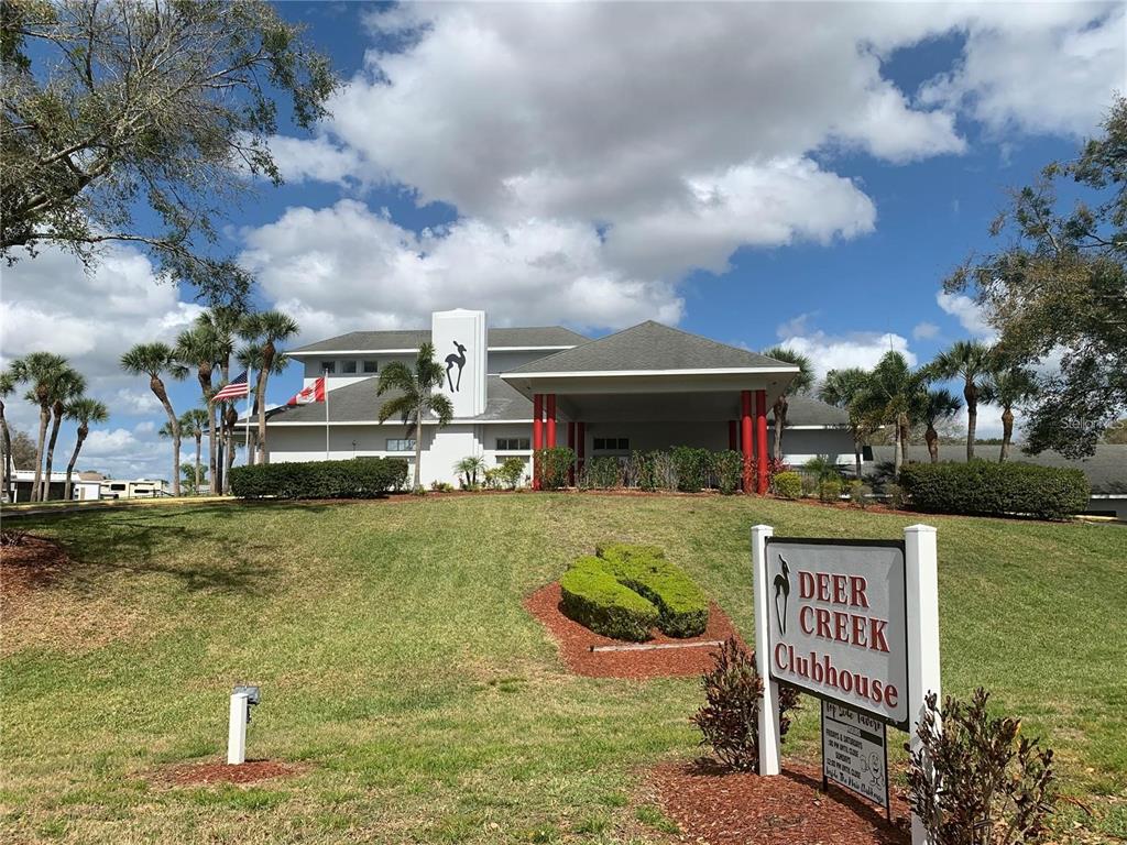 The exterior of the Deer Creek Clubhouse features a large lawn, palm trees, and flags — 319 BROKEN WOODS BOULEVARD, DAVENPORT, FL