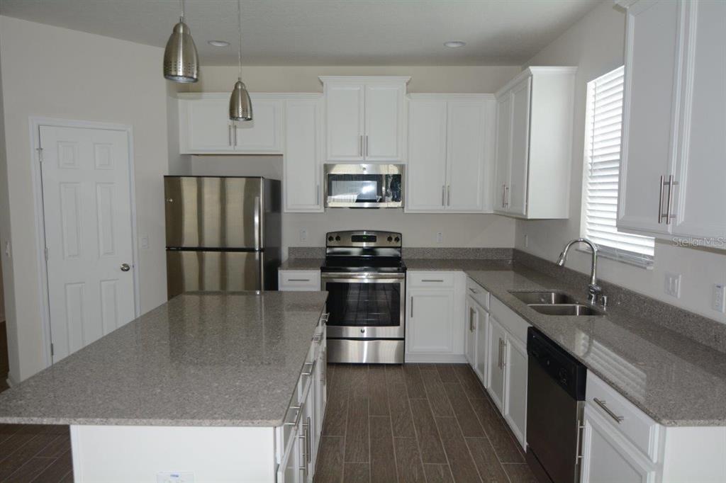 A kitchen with white cabinets, stainless steel appliances, a granite island, and wood-look tile flooring — 8104 PLEASANT PINE CIRCLE, WINTER PARK, FL