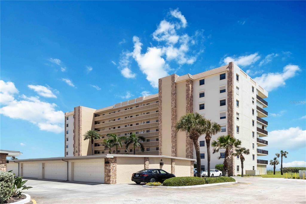 A multi-story apartment building with balconies and a detached garage structure under a blue sky — 1890 N ATLANTIC AVENUE UNIT A403, COCOA BEACH, FL