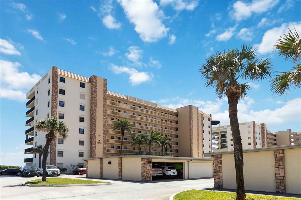 A multi-story apartment building with a parking garage and palm trees under a blue sky — 1890 N ATLANTIC AVENUE UNIT A403, COCOA BEACH, FL