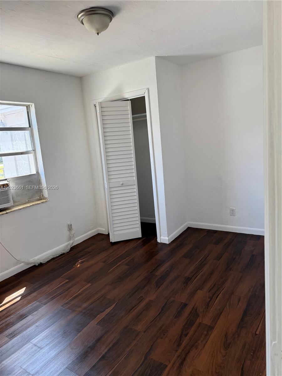 A bedroom features dark wood-look flooring, white walls, a closet with louvered doors, and a window — 3810 SW 25th St # 1, West Park FL 33023, WEST PARK, FL