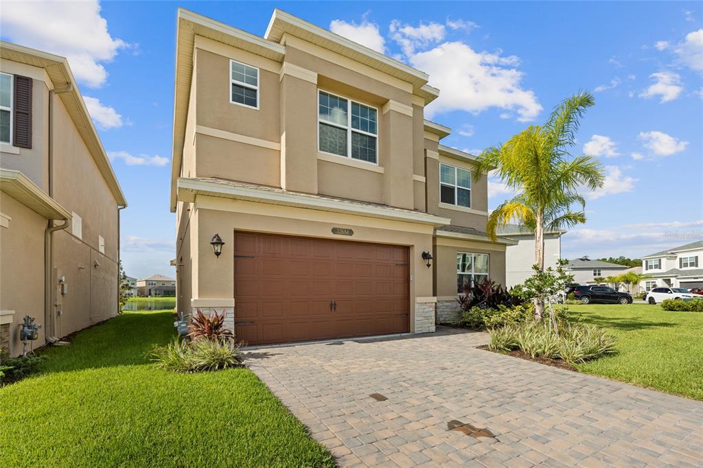 A two-story tan stucco house features a brown garage door and a paved driveway — 32684 TAMARIND GROVE LANE, WESLEY CHAPEL, FL