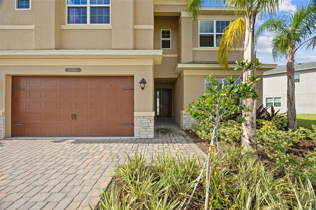 A two-story house exterior features a brown garage door, stone accents, and a paved driveway — 32684 TAMARIND GROVE LANE, WESLEY CHAPEL, FL