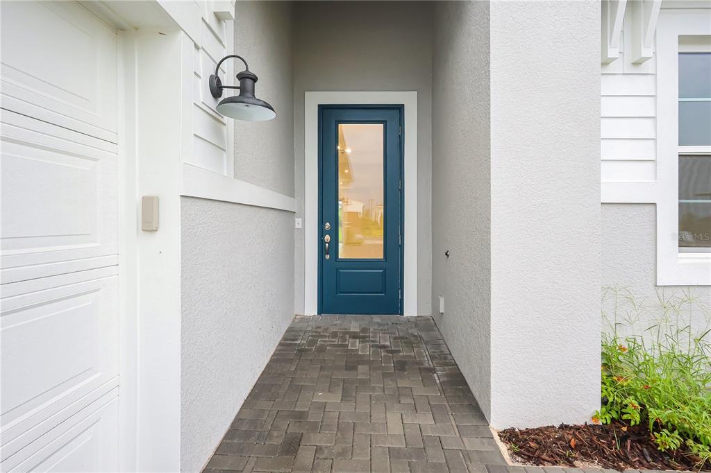 A blue front door with a glass panel sits at the end of a paved walkway — 1618 BELLAGIO LOOP, TAVARES, FL