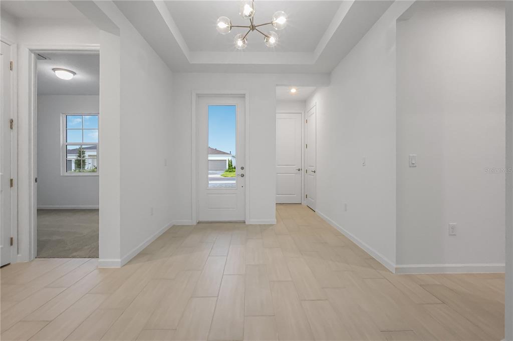 A bright entryway features light-colored tile flooring, a tray ceiling with a chandelier, and a front door — 1618 BELLAGIO LOOP, TAVARES, FL