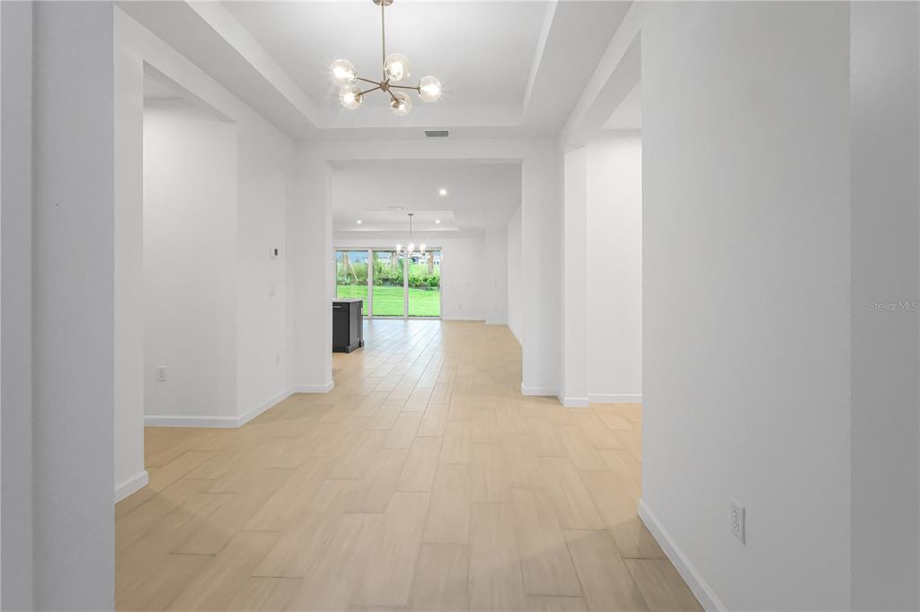 A bright, open-concept interior features light wood-look tile flooring and two modern globe chandeliers — 1618 BELLAGIO LOOP, TAVARES, FL
