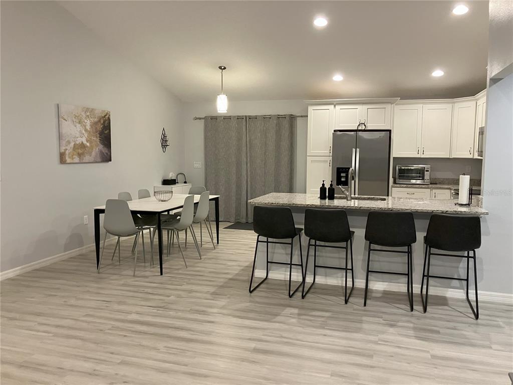 A kitchen and dining area features white cabinets, a granite island, and light wood flooring — 5415 SW 153RD PLACE ROAD, OCALA, FL