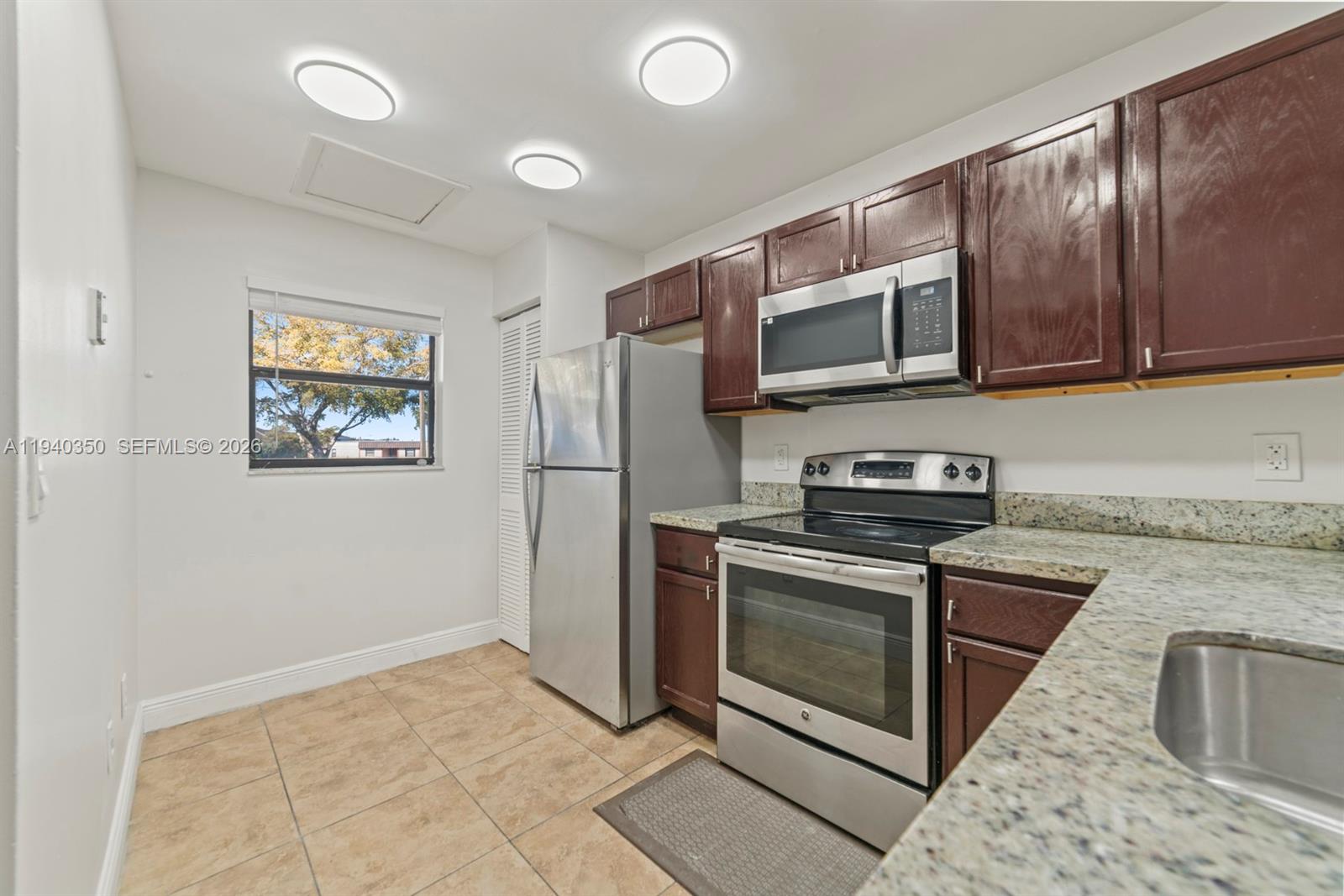 A kitchen features dark wood cabinets, stainless steel appliances, granite countertops, and tile flooring — 880 NE 207th Ter # 10, Miami FL 33179, MIAMI, FL