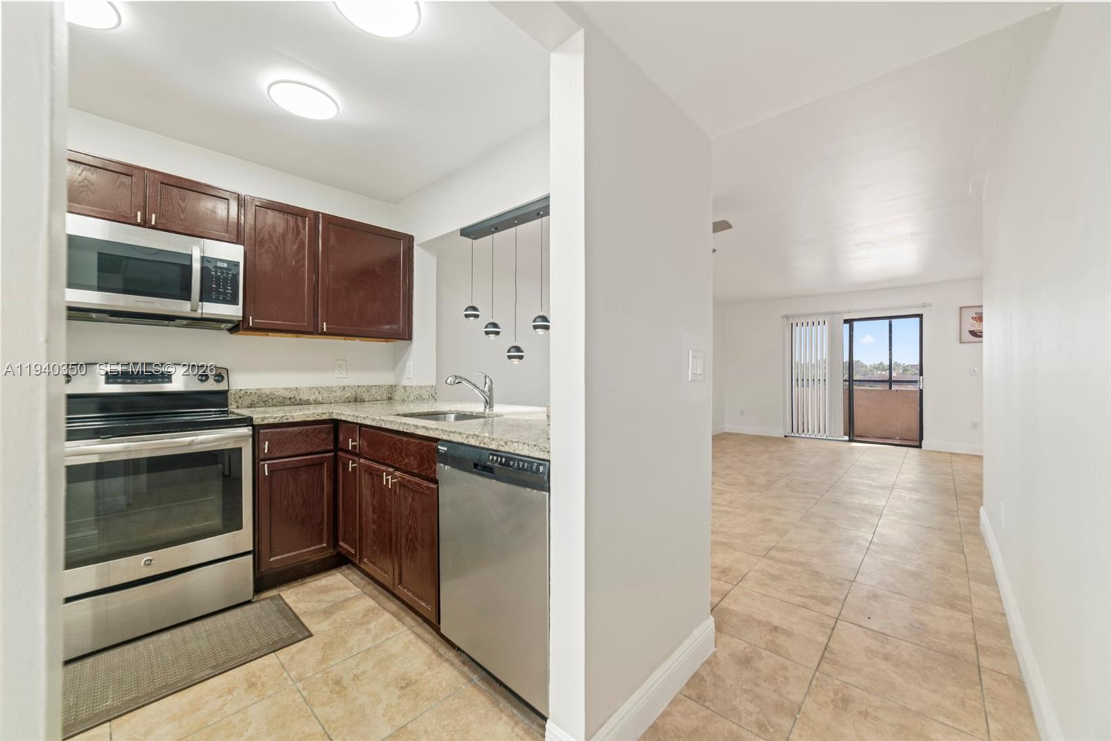A kitchen with dark wood cabinets and stainless steel appliances opens into a living area — 880 NE 207th Ter # 10, Miami FL 33179, MIAMI, FL