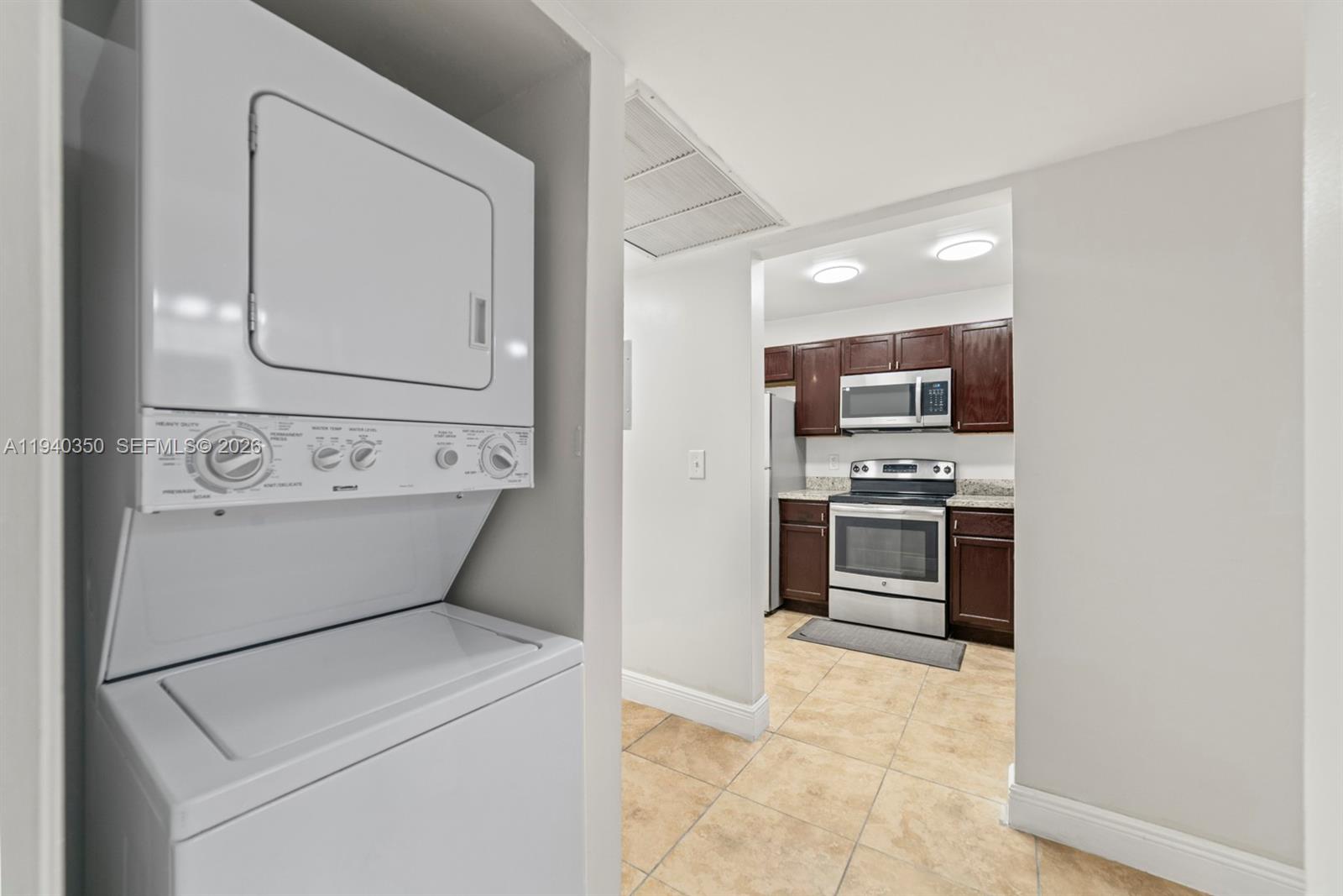 A stacked washer and dryer unit sits in a closet next to a kitchen — 880 NE 207th Ter # 10, Miami FL 33179, MIAMI, FL