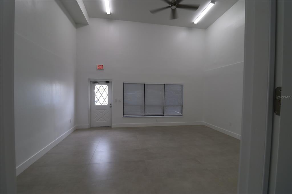 A bright, empty room features high ceilings, white walls, tile flooring, and an exit door — 1225 TAMIAMI TRAIL UNIT A8, PORT CHARLOTTE, FL
