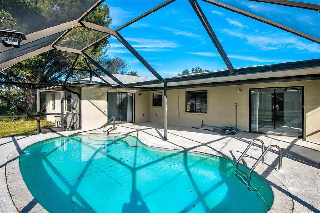 A swimming pool with a metal ladder sits inside a screened-in patio enclosure — 838 JARVIS STREET, PORT CHARLOTTE, FL