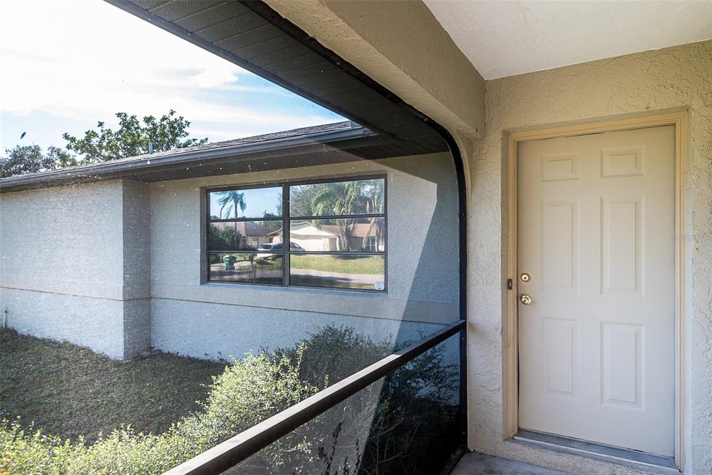 A beige door sits next to a window on a covered porch with screen enclosure — 838 JARVIS STREET, PORT CHARLOTTE, FL